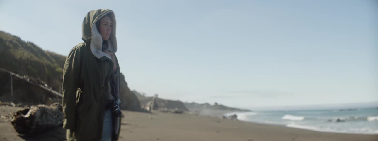 Woman is standing on beach wearing hooded jacket