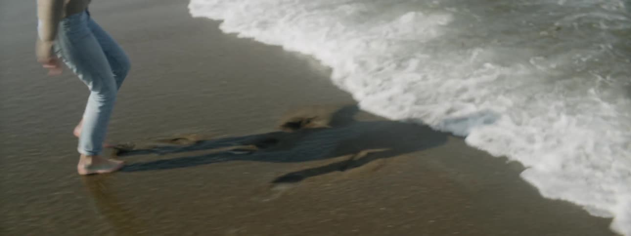 A woman is moving backwards away from the tide as it comes in on a beach