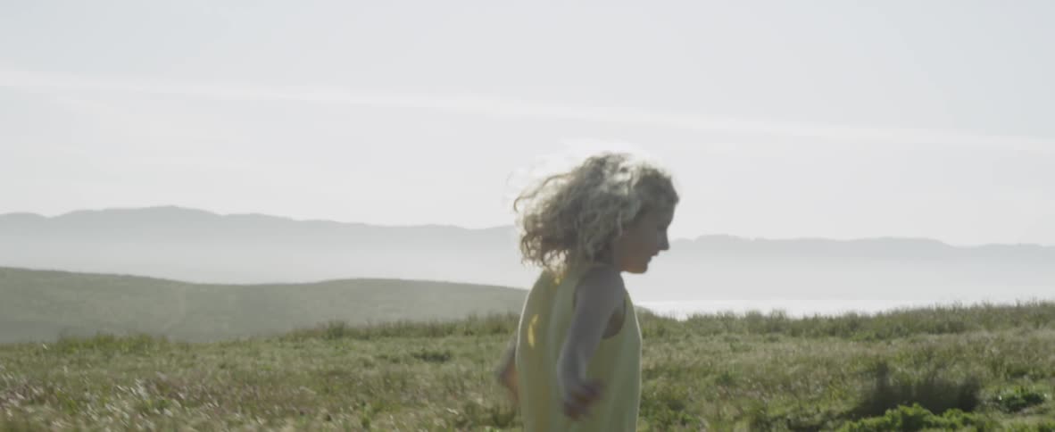 A young girl runs playfully through a grass field