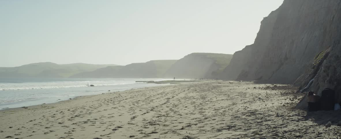 Waves come to shore on a sandy beach surrounded by hills