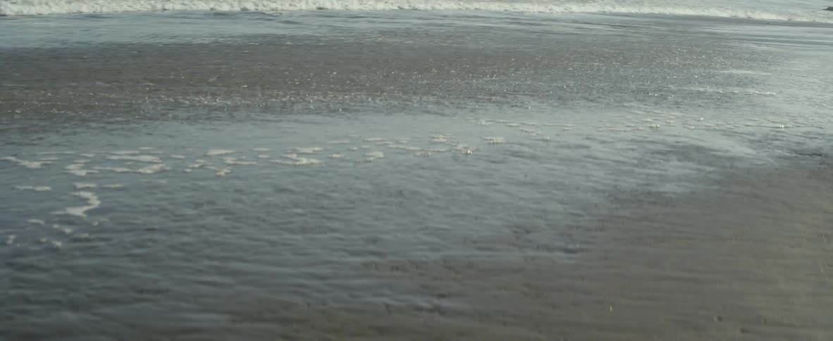 Ocean water flowing onto beach leaving foamy bubbles in the sand