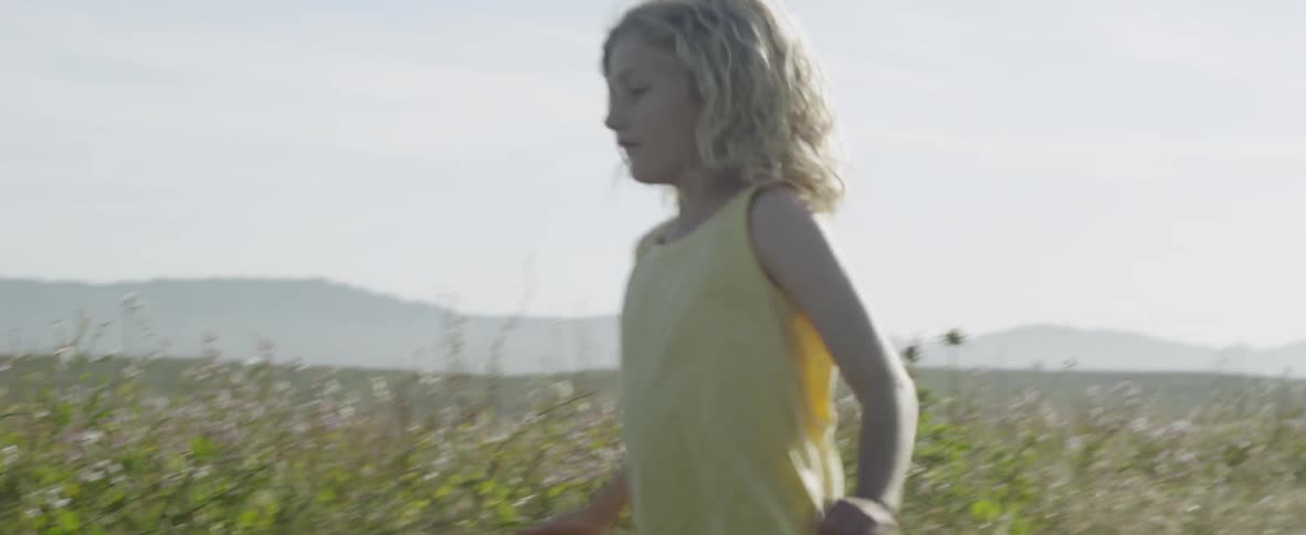 A young girl runs playfully through a grass field