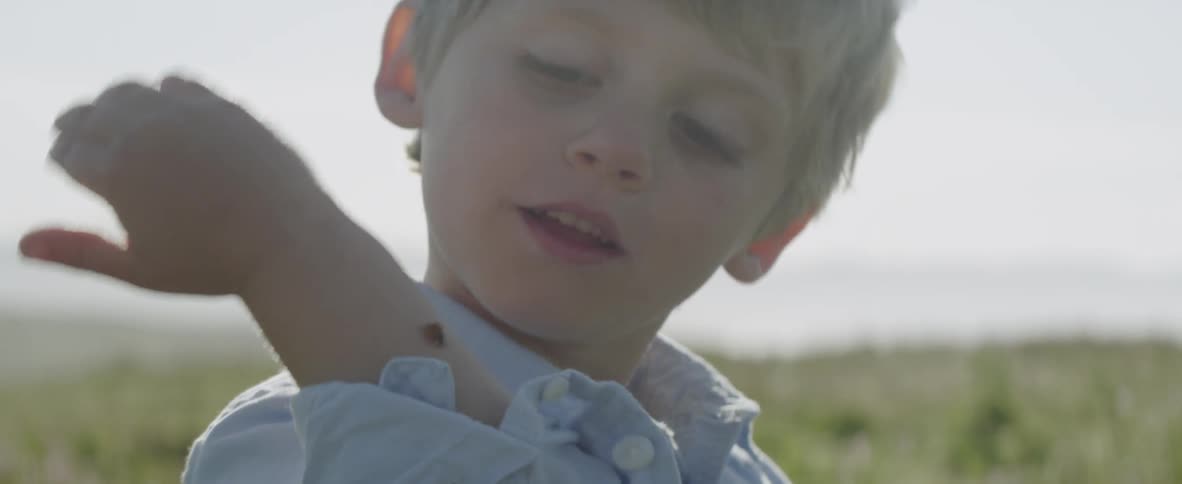A boy is watching a ladybug as it crawls over his arm outside during the day