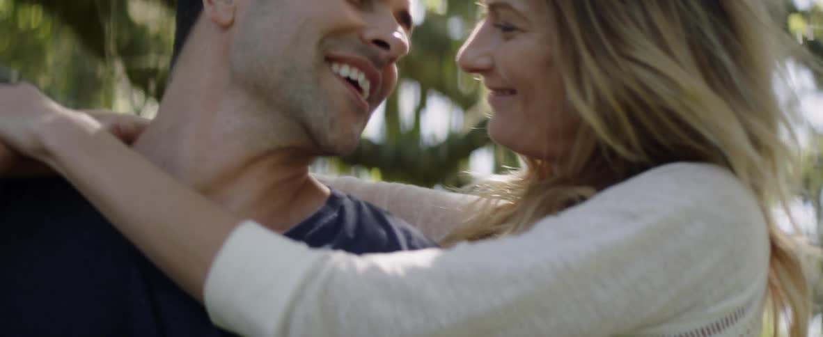Man and woman embrace outside near trees on sunny day