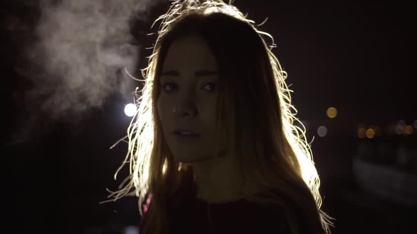 A woman standing and staring with a light and the city in the background