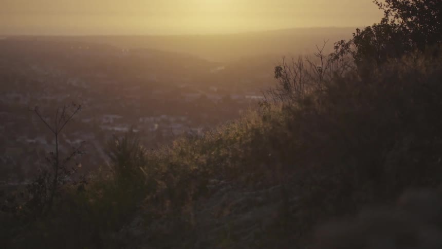 A hill overlooking a town with the sky and the sun in the background