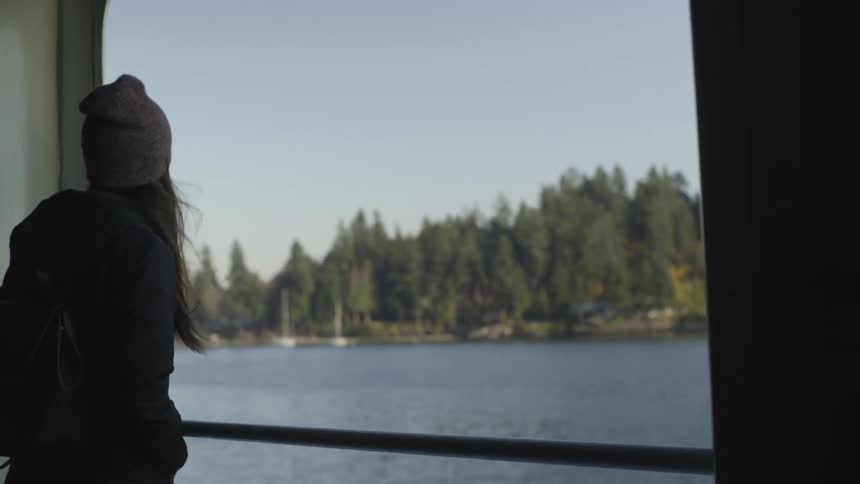 Woman stands on the side of a boat looking at the water with her hair blowing in the wind
