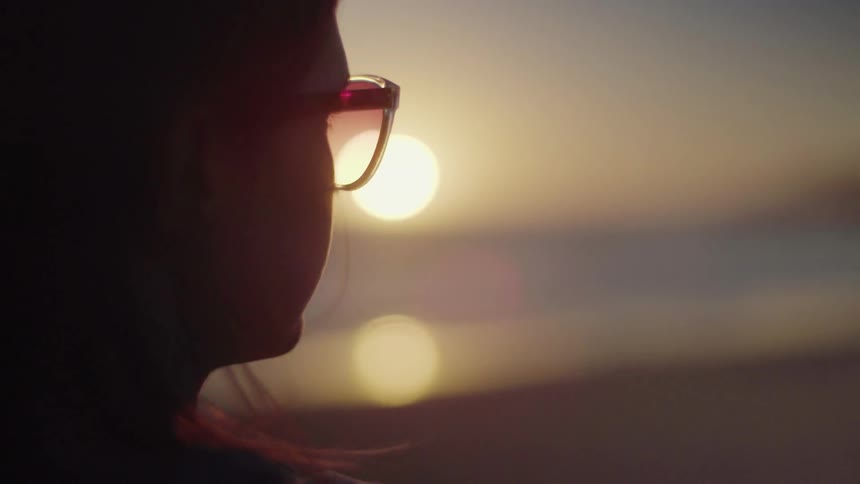 A woman stands on a beach at sunset