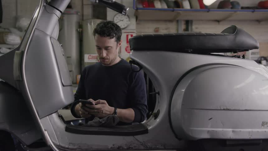 Man types on a phone while looking at a small motorbike