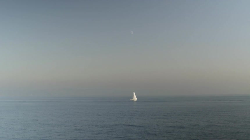 A sailboat is sailing across the ocean on a hazy day