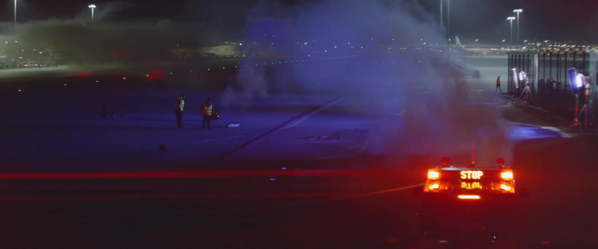 Workers mill about near a plume of smoke at an airport at night
