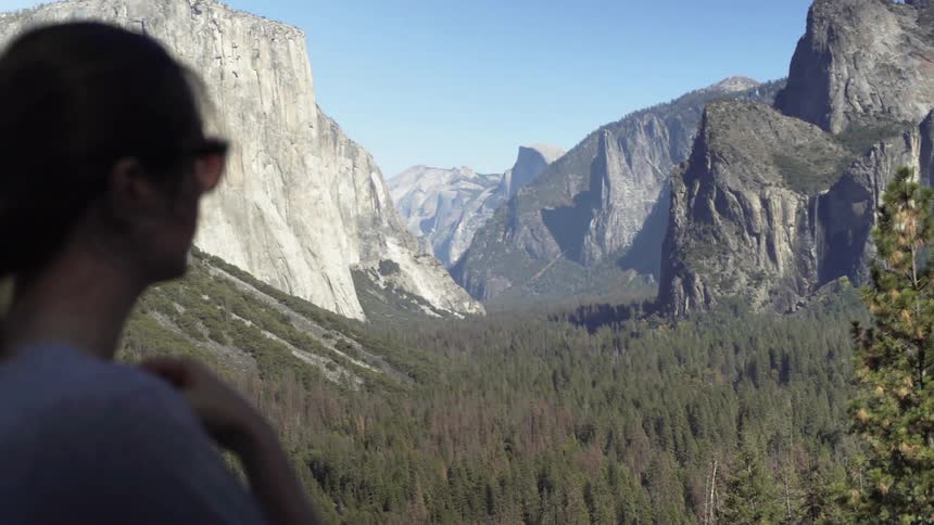 A woman is turning and walking away from a view in yosemite on a sunny day