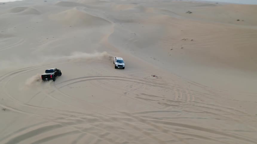 Two trucks spin cookies in a desert