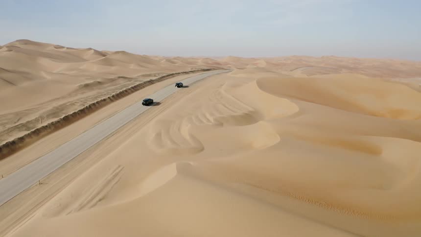 Two vehicles driving on a paved road through a desert area