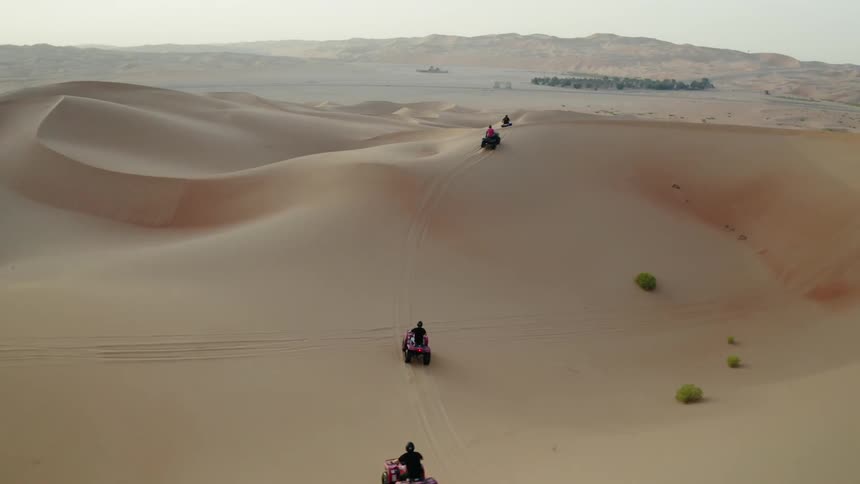 People drive four wheelers over sandy hilly desert
