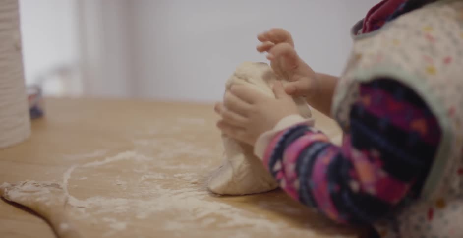 A young girl kneads dough in a kitchen