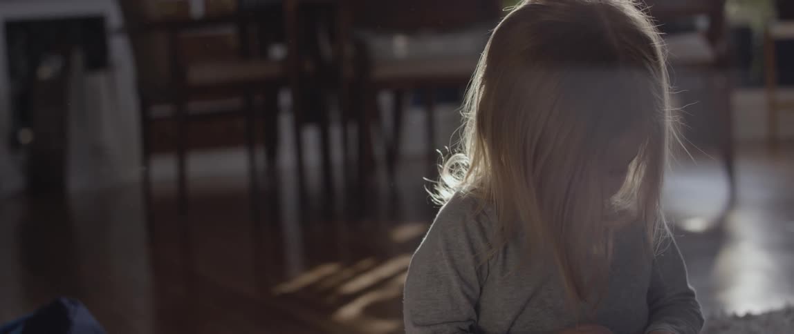 The sun shines on a girls hair as she plays on the floor