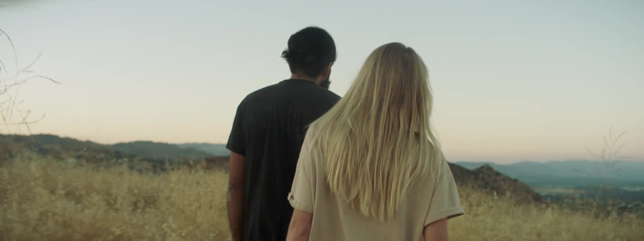 A man and woman walk in a rural field at sunset
