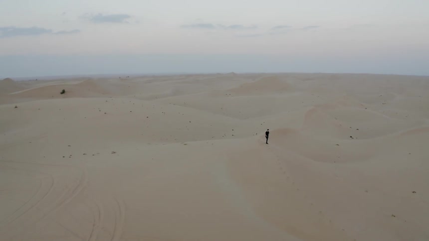 A man is standing atop a sand dune in a desert near dusk