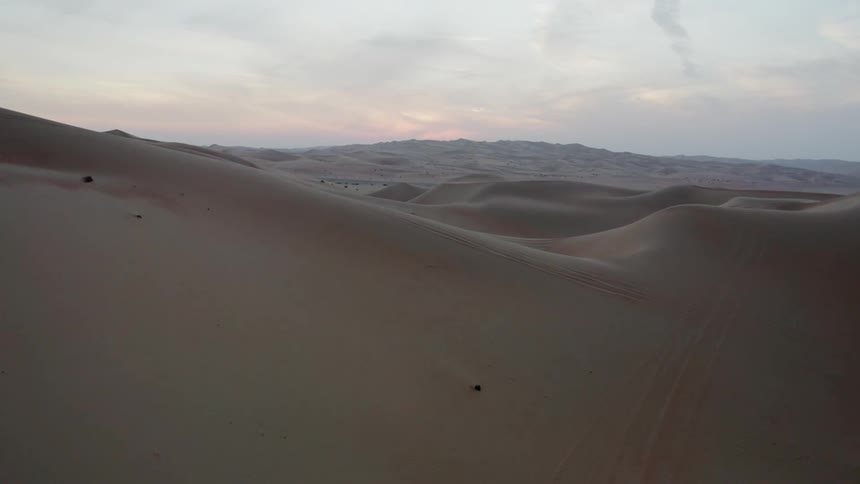Sand dunes cover a desert landscape at sunset