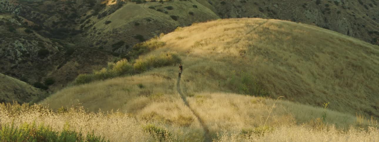 Two people walk on a narrow trail on a grassy hill