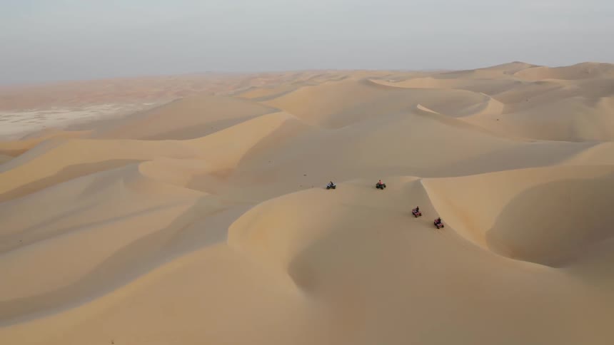 People drive four wheelers over sandy hilly desert