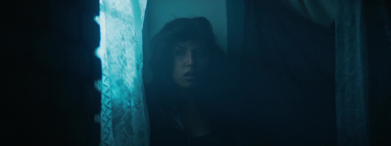 Woman hides next a window while lights flash outside