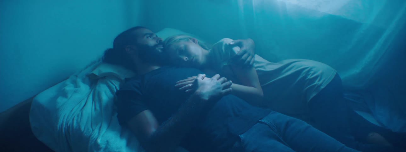 A searchlight is passing through a window over a couple resting in a bed
