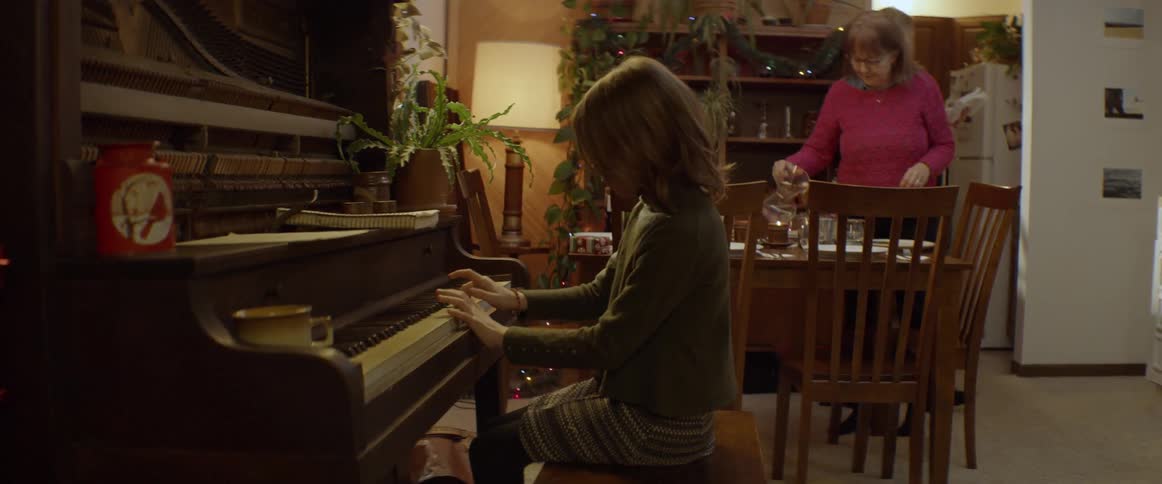 Young girl plays the piano as two women set the table for dinner