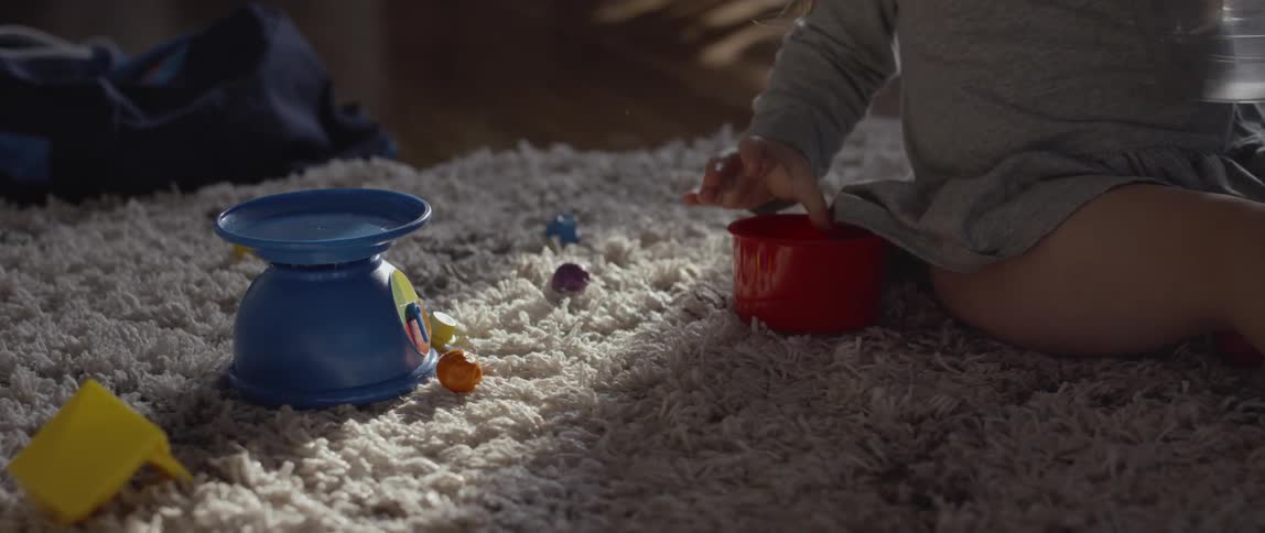 Child plays with marbles on a rug putting them into a cup