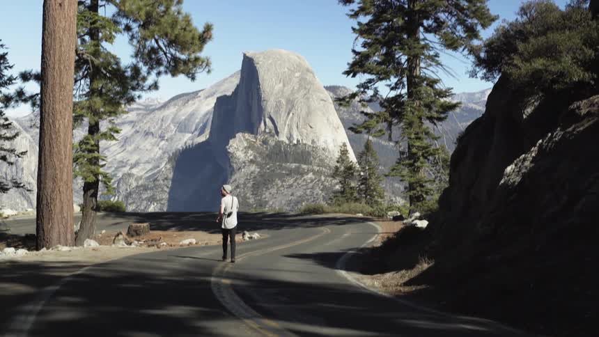 A man walks on a mountain road with a camera