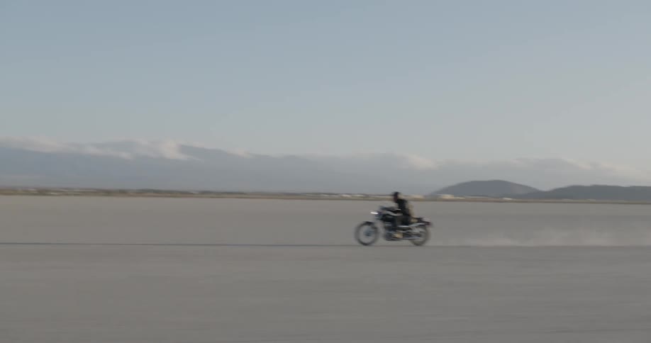 A man is riding a motorcycle across a salt flat on a sunny day