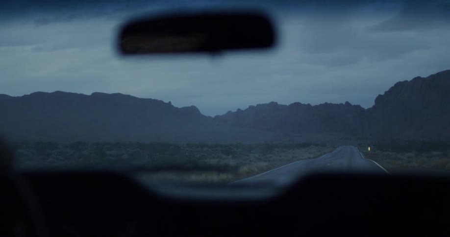 A car drives towards mountains on a rural road