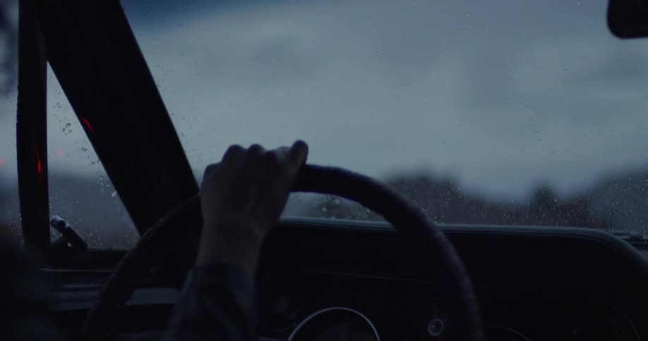 A car drives on a rural road in the rain