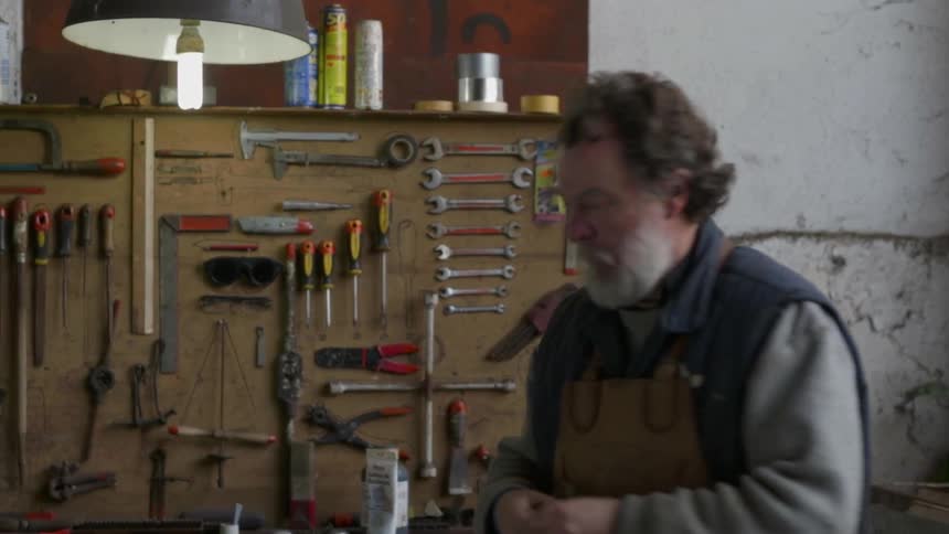 A man grabs a tool from his bench