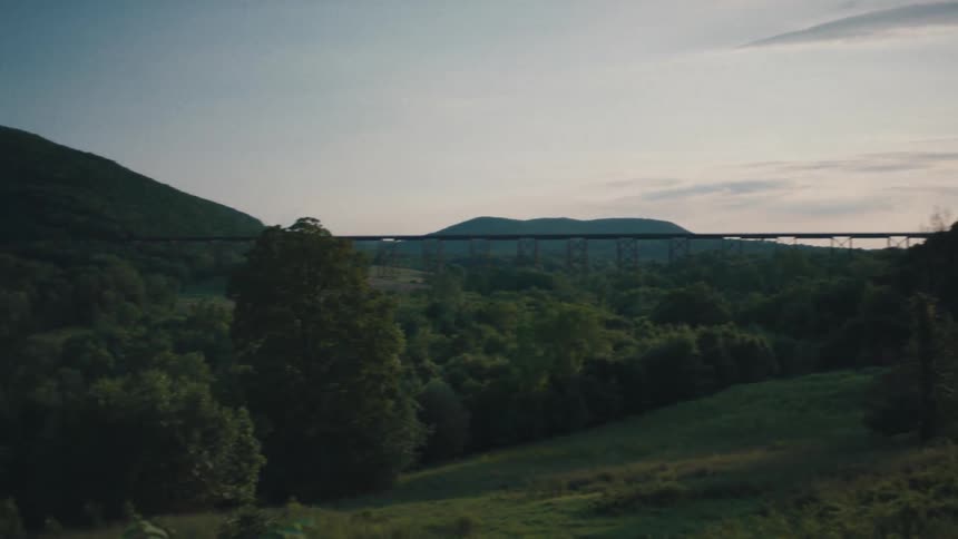 Sun shines over tree covered land and hills