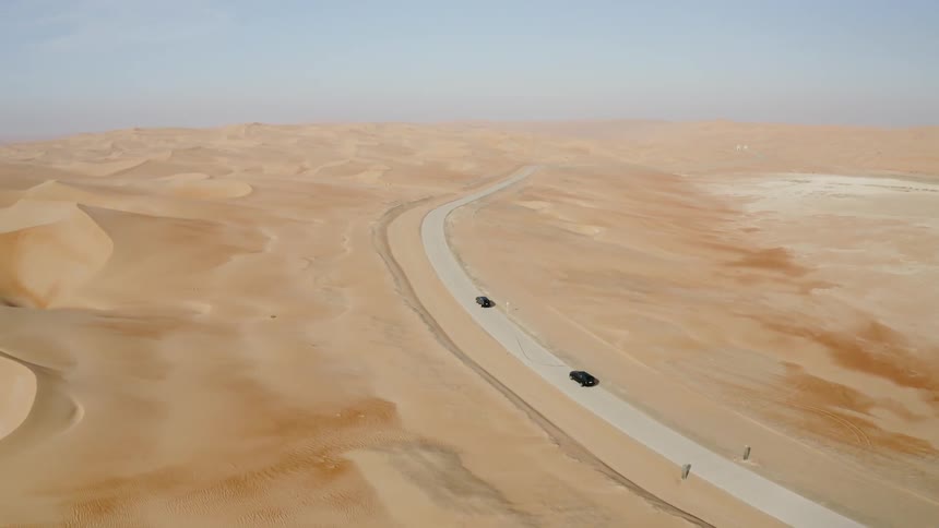 Two vehicles drive on a winding desert road