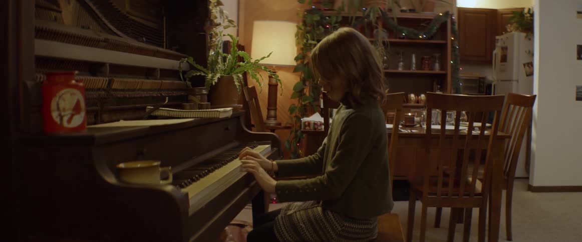 A girl is practicing piano inside a home in the evening