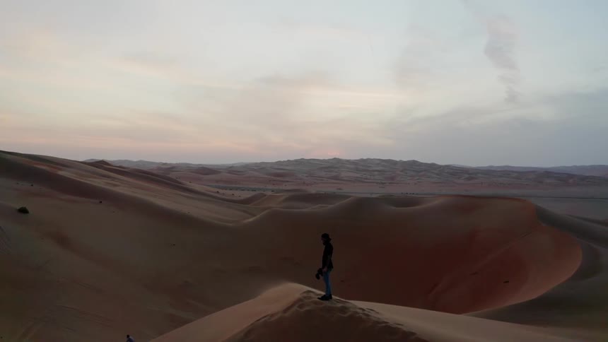 A hiker stands on a sand dune in a desert at sunset