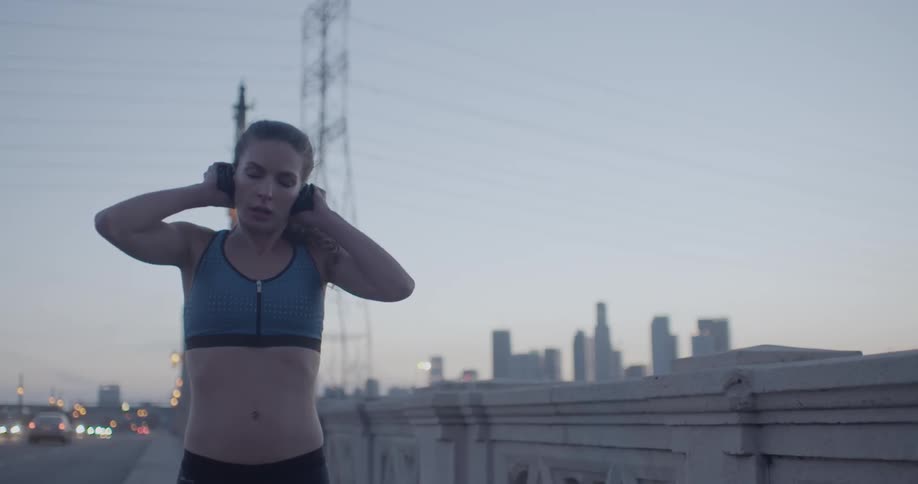 Woman taking off her headphones while standing on a city street as she is out exercising