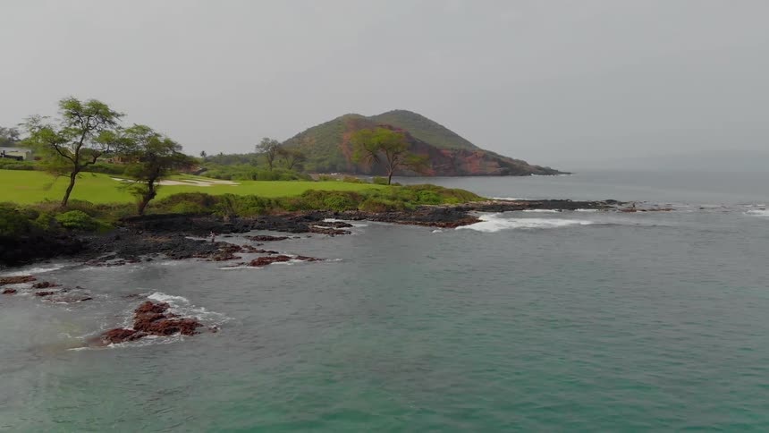 Waves are rolling onto rocks on a tropical shore during the daylight