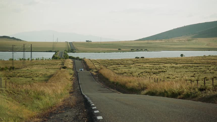 Car travels down a hilly road between 2 fields