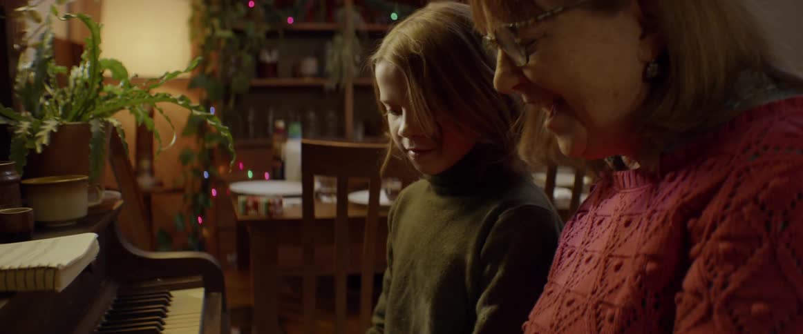 A woman sits beside a child on a piano bench teaching him to play