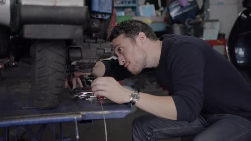 A man is working on a moped inside a garage in daylight