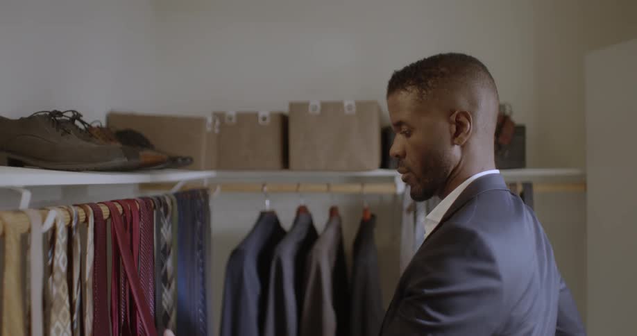 Man walks into a closet and looks at ties