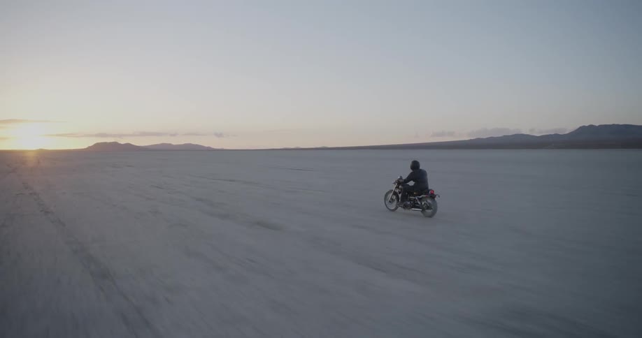 Person riding motorcycle on sandy flatland wilderness at sunset