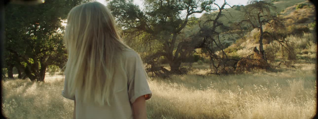 A man follows a woman as they walk in the grass