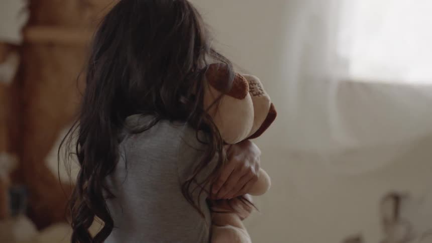 A little girl is hugging a stuffed toy inside a room in daylight