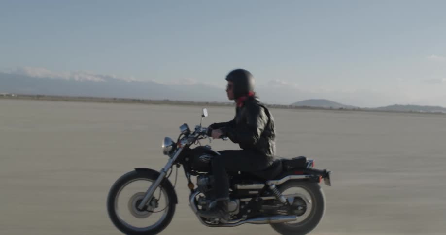 A man stands up then sits back down while driving a motorcycle