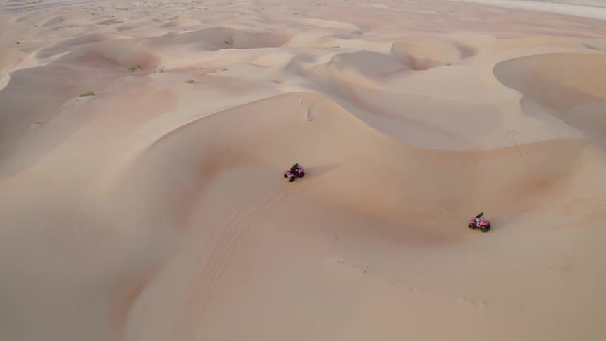 People are riding atvs over sand dunes in daylight